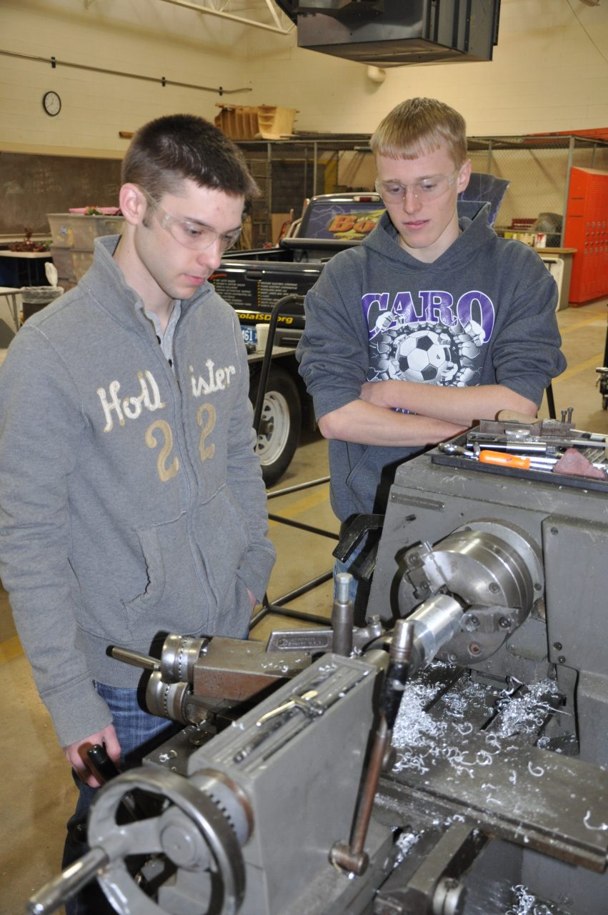 The students manufacture a part for the custom pedal car's suspension system.
