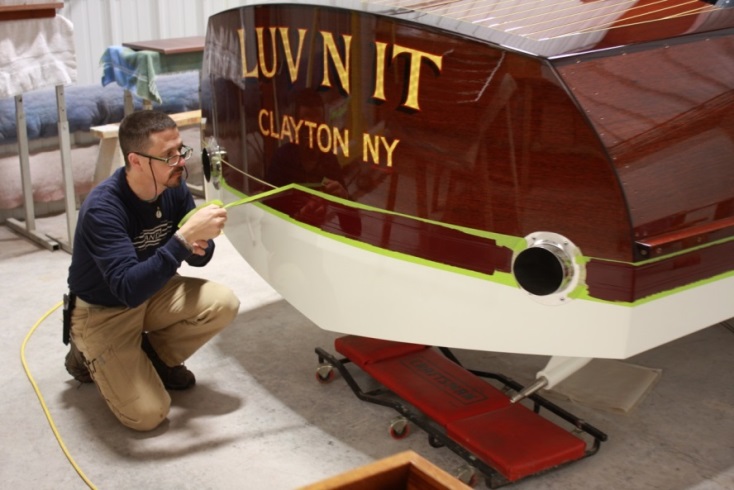 revor Brazell pulls the tape on a freshly painted waterline. The boat’s name gleams under the new clear coat.