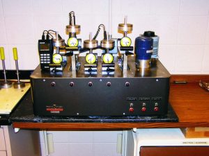 This test apparatus is used to determine the effects of high temperatures on cured epoxy. It holds multiple test samples in a bath of heated oil while a three-point load is applied to the samples.